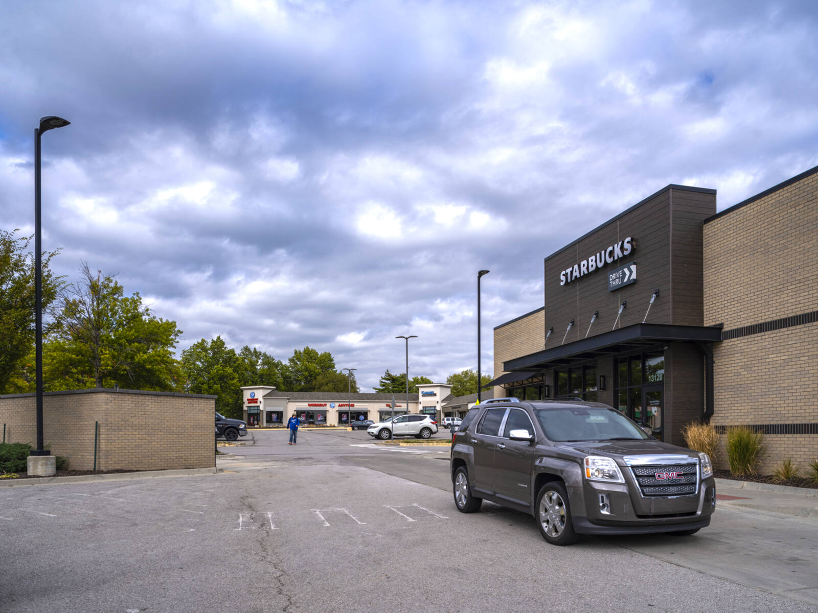 GMC SUV passing Starbucks drive-thru with trees and people in background.