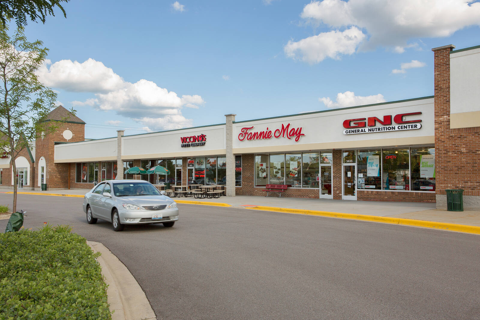 Grey car driving past GNC nutrition store and inline shops at Butterfield Square.