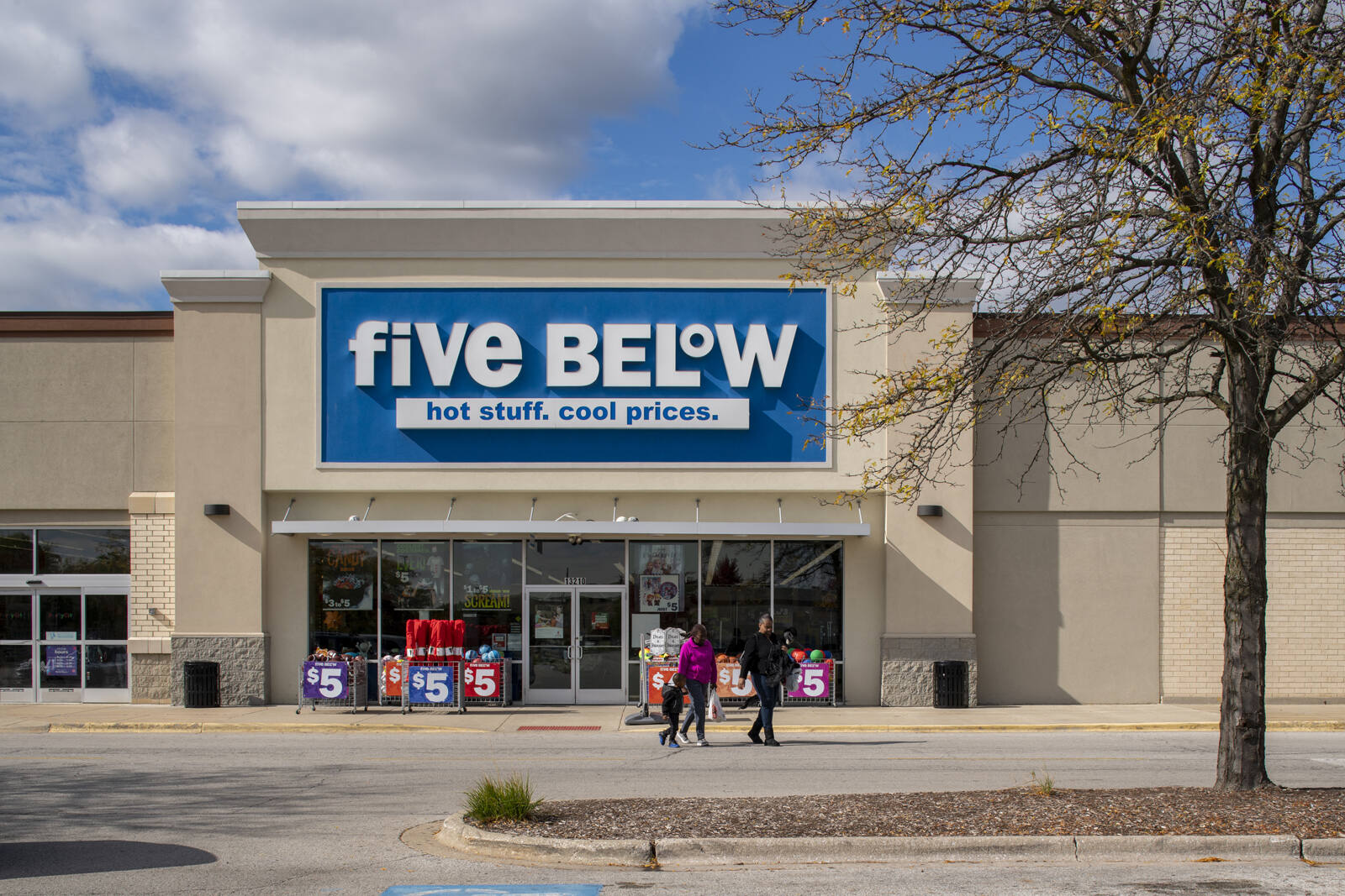 Tree on the right side of entrance to Five Below with three people walking towards entrance