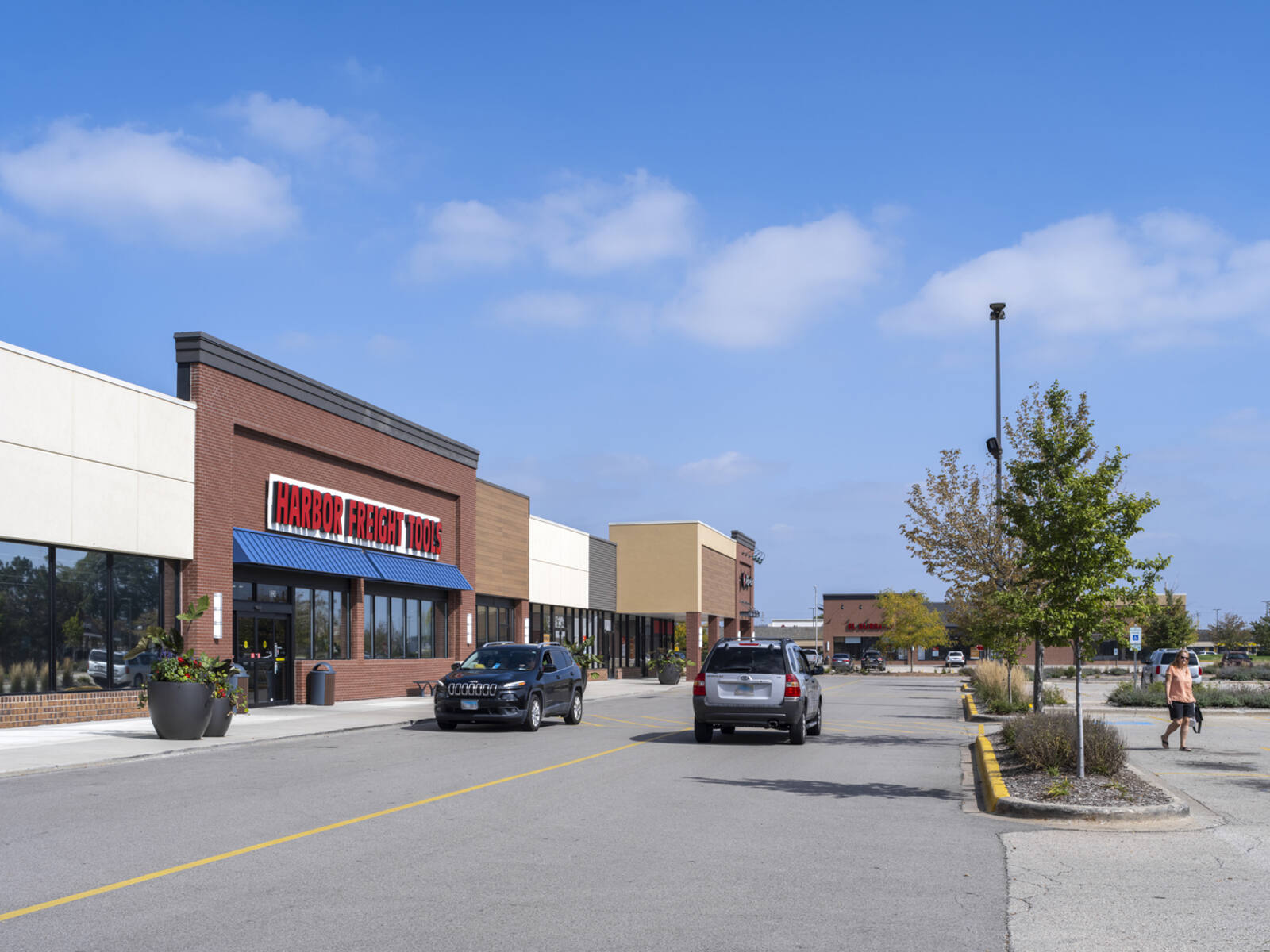 2 cars passing a Harbor Freight Tools store on access road with tree planter on the right.