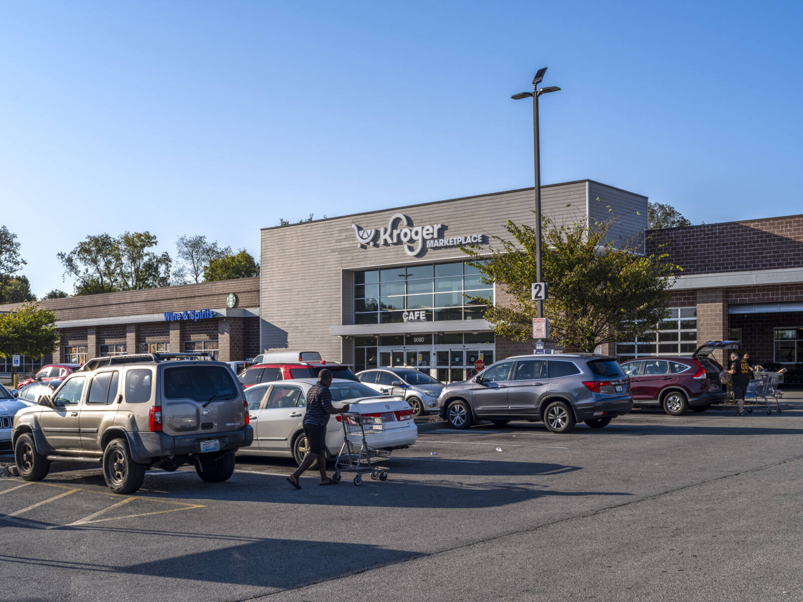 Patrons with carts approach and unload cars in parking lot of Kroger.