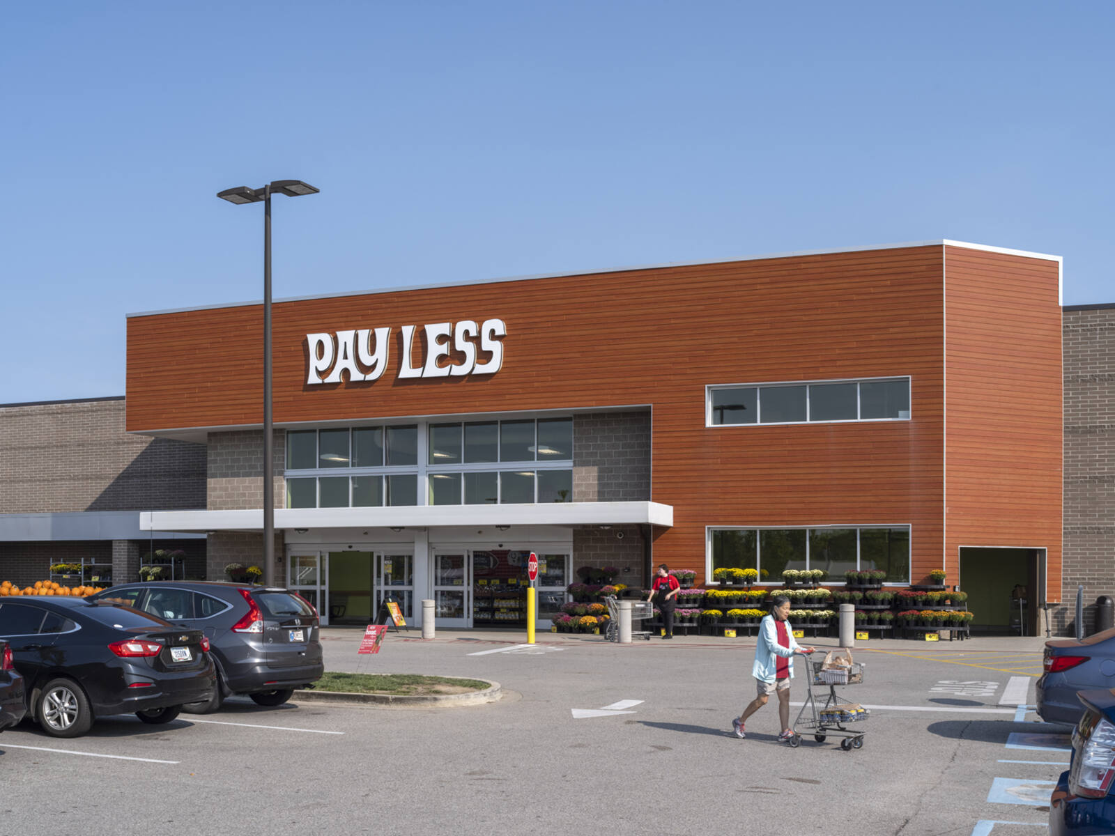 Woman with cart in parking lot of Pay Less grocery store.