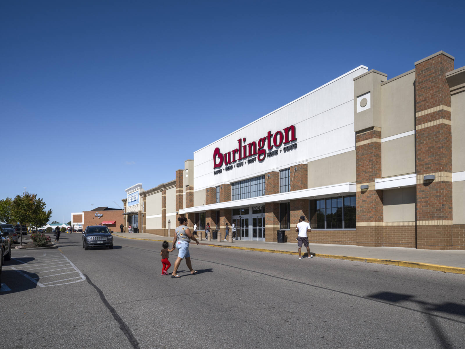 Patrons in crosswalk for Burlington store with cars on road in the background.