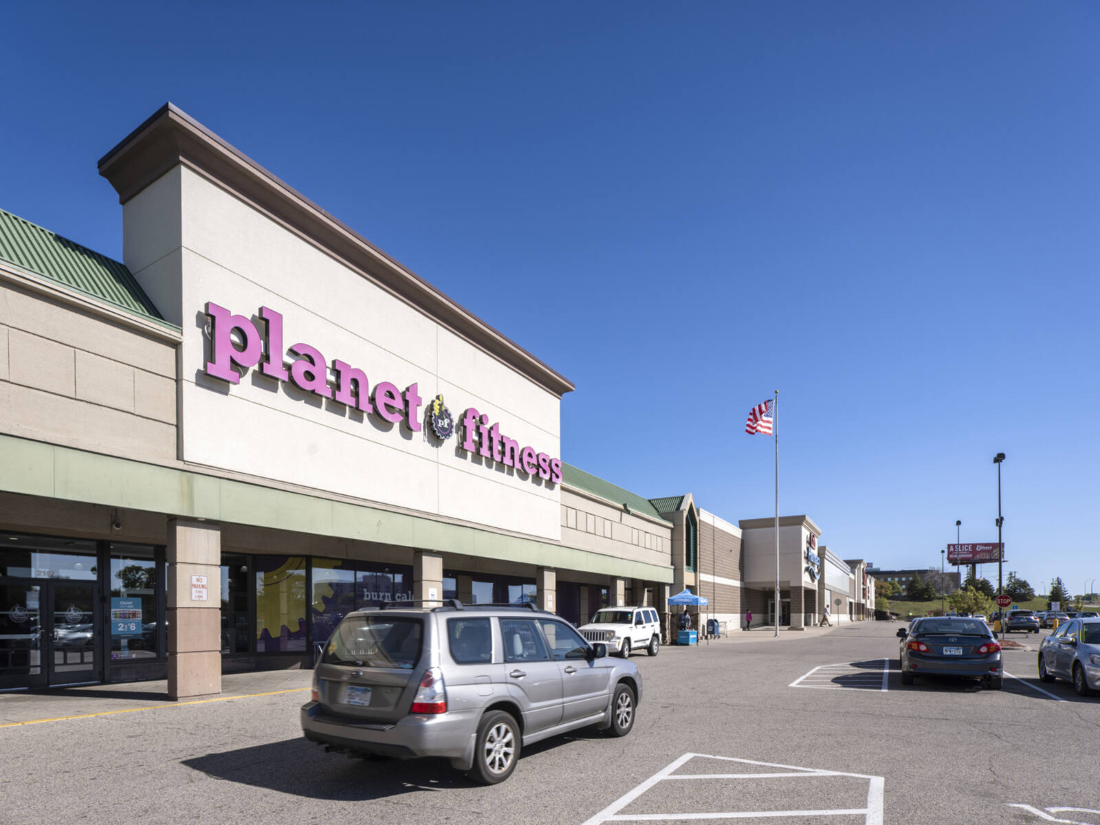 Grey SUV in front of Planet Fitness gym with parking lot in background.