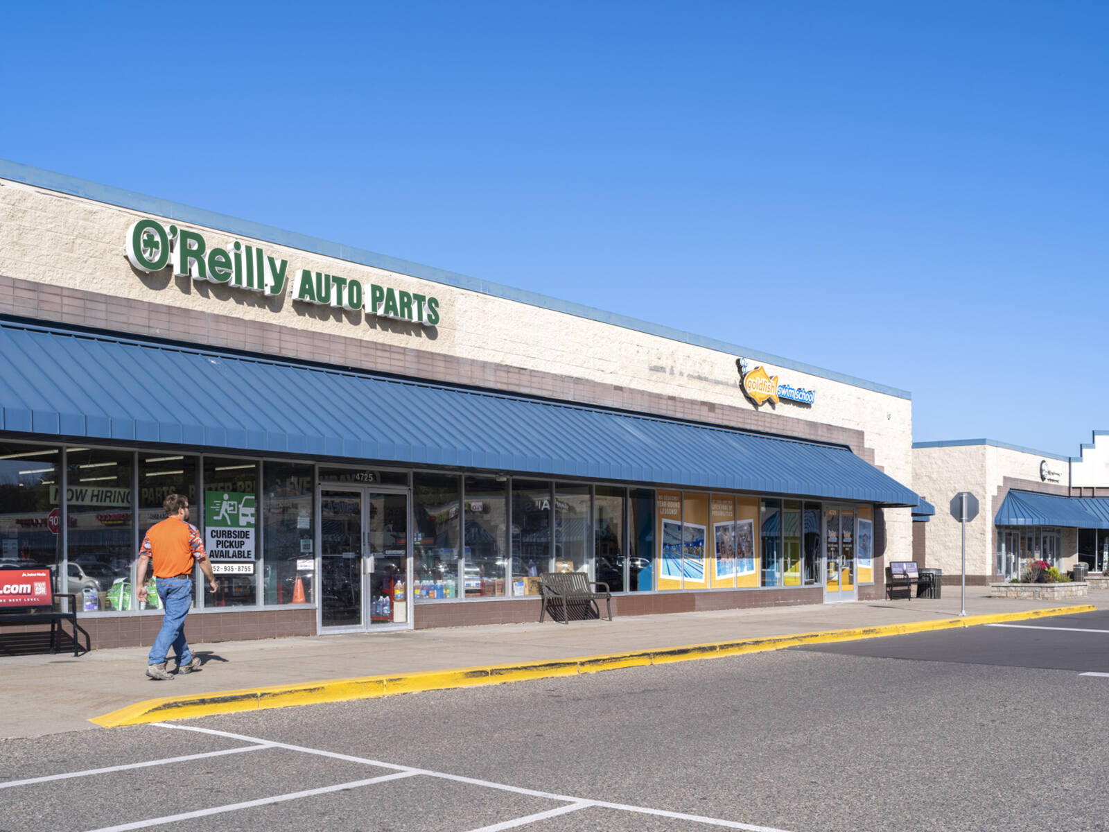 Man entering O'Reilly Auto Parts on sidewalk from parking lot.