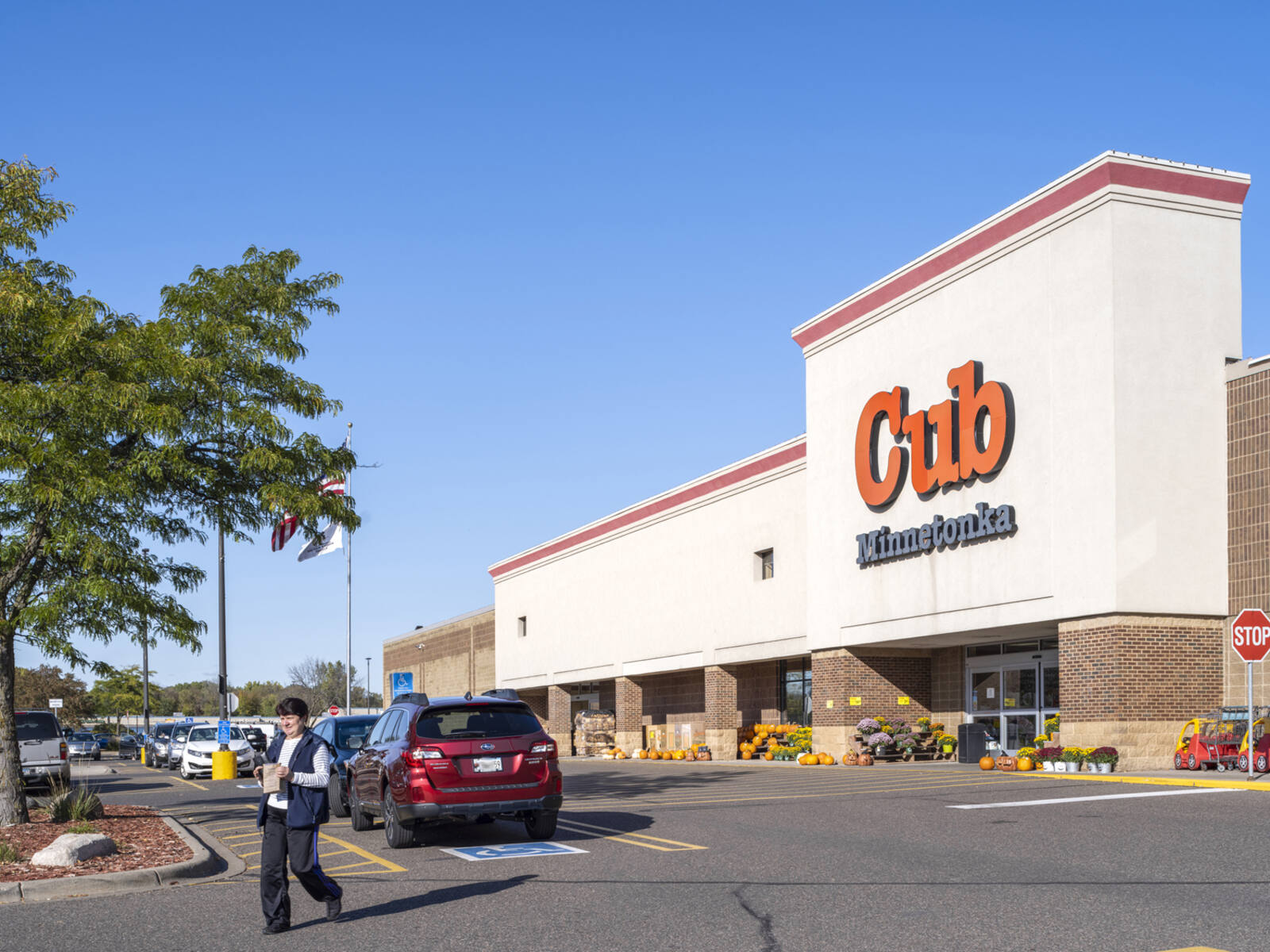 Woman exiting Cub Foods to parking lot with cars in back of her.
