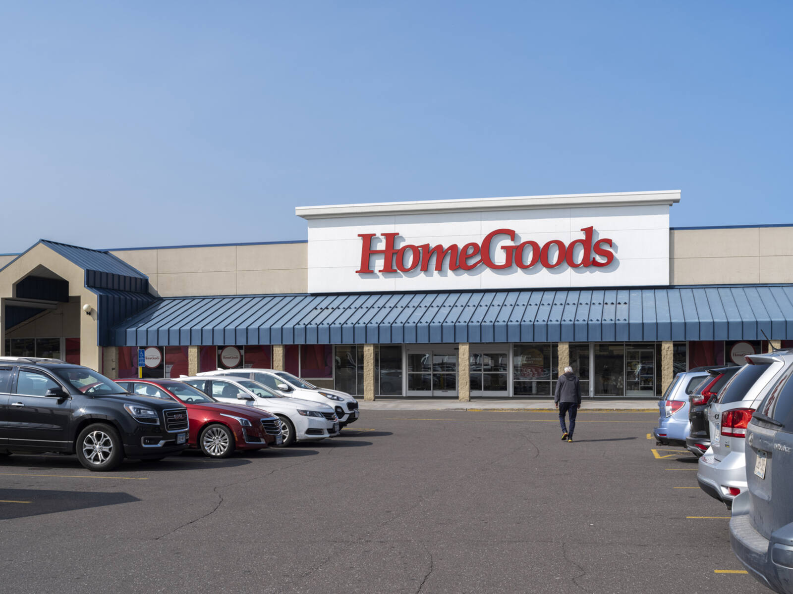 Pedestrian walking towards HomeGoods via the busy parking lot.