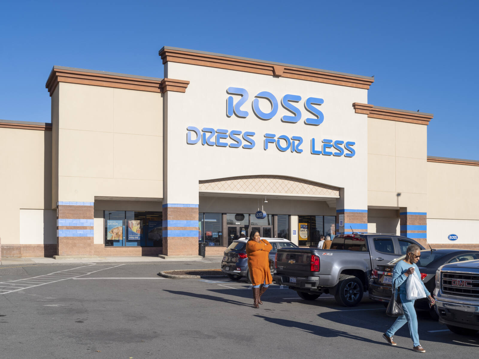 People walk in front of aisle of parked cars at Ross Dress for Less.
