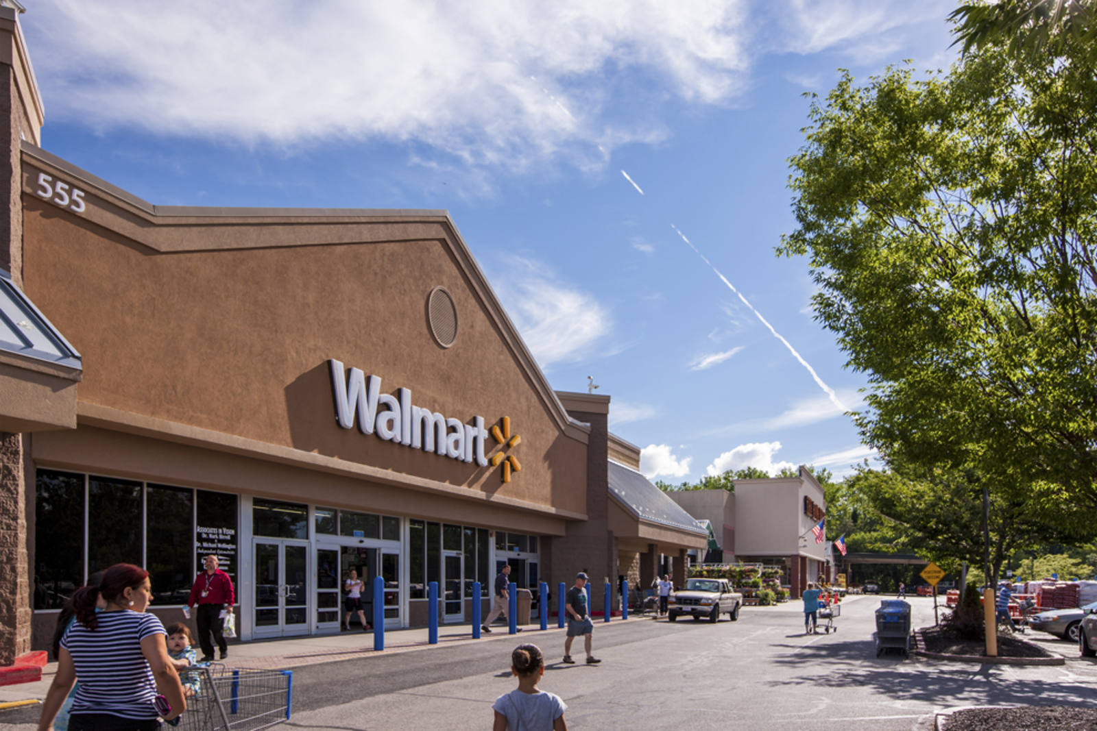 Customers entering and exiting Walmart in a tree-lined parking lot at Berkshire Crossing.