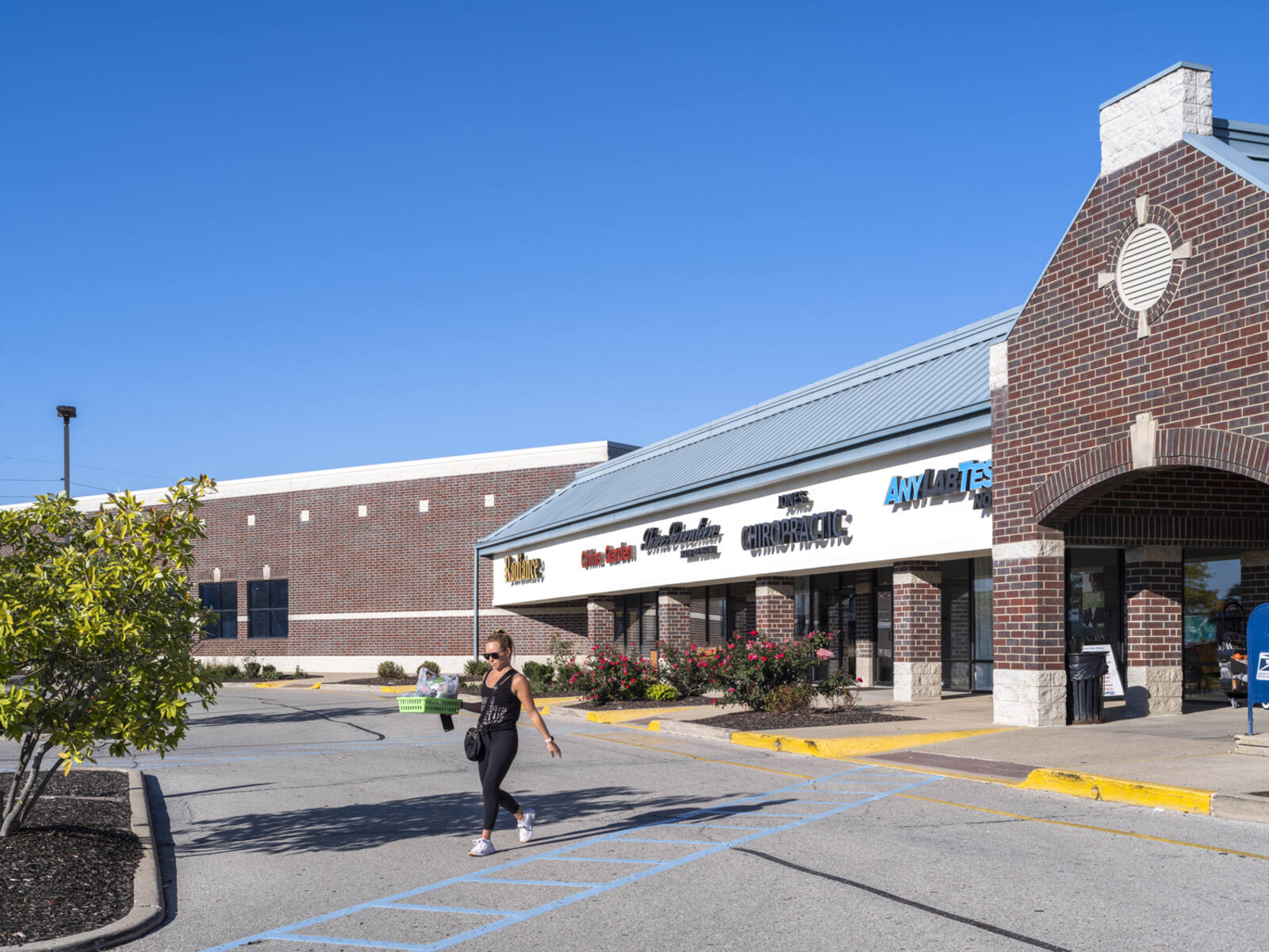 Woman crossing road in front of inline shops at shopping center.