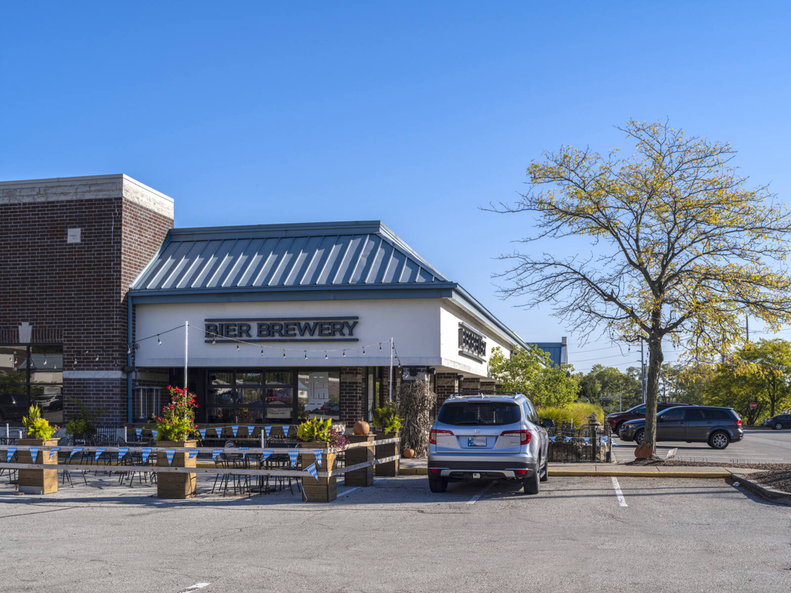 Bier Brewery with tree on the right and car in front parking lot with outdoor seating on left.