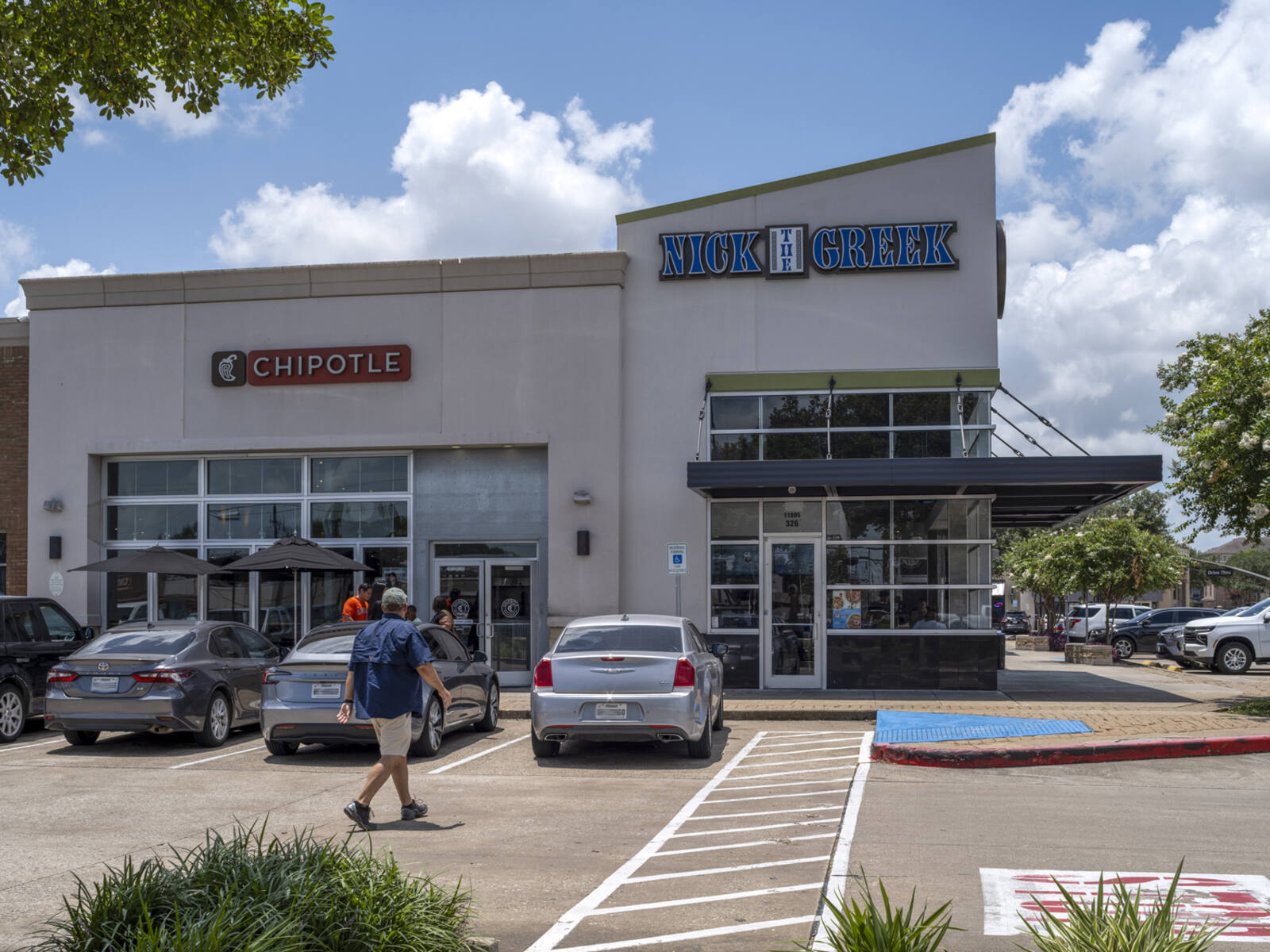 Cars and man in lot for Chipotle and Nick the Greek restaurants.