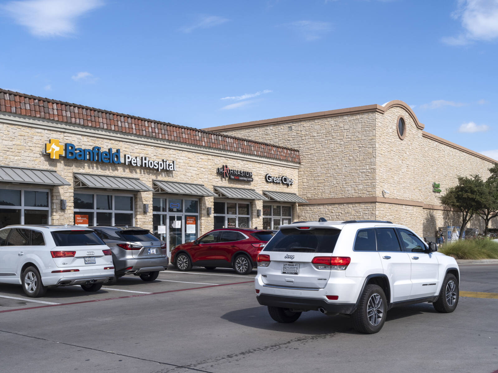 White SUV passing Banfield Pet Hospital on access road in shopping center.