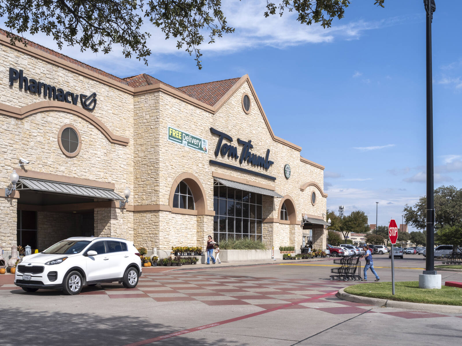 Customer with cart and white SUV in crosswalk of Tom Thumb grocery store.