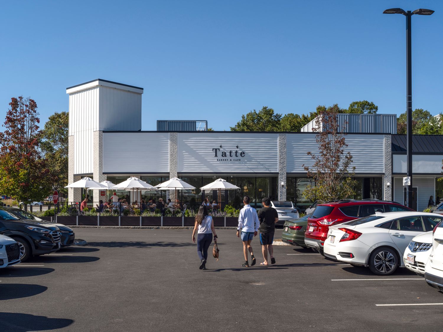 People approach Tatte restaurant through parking lot aisle.