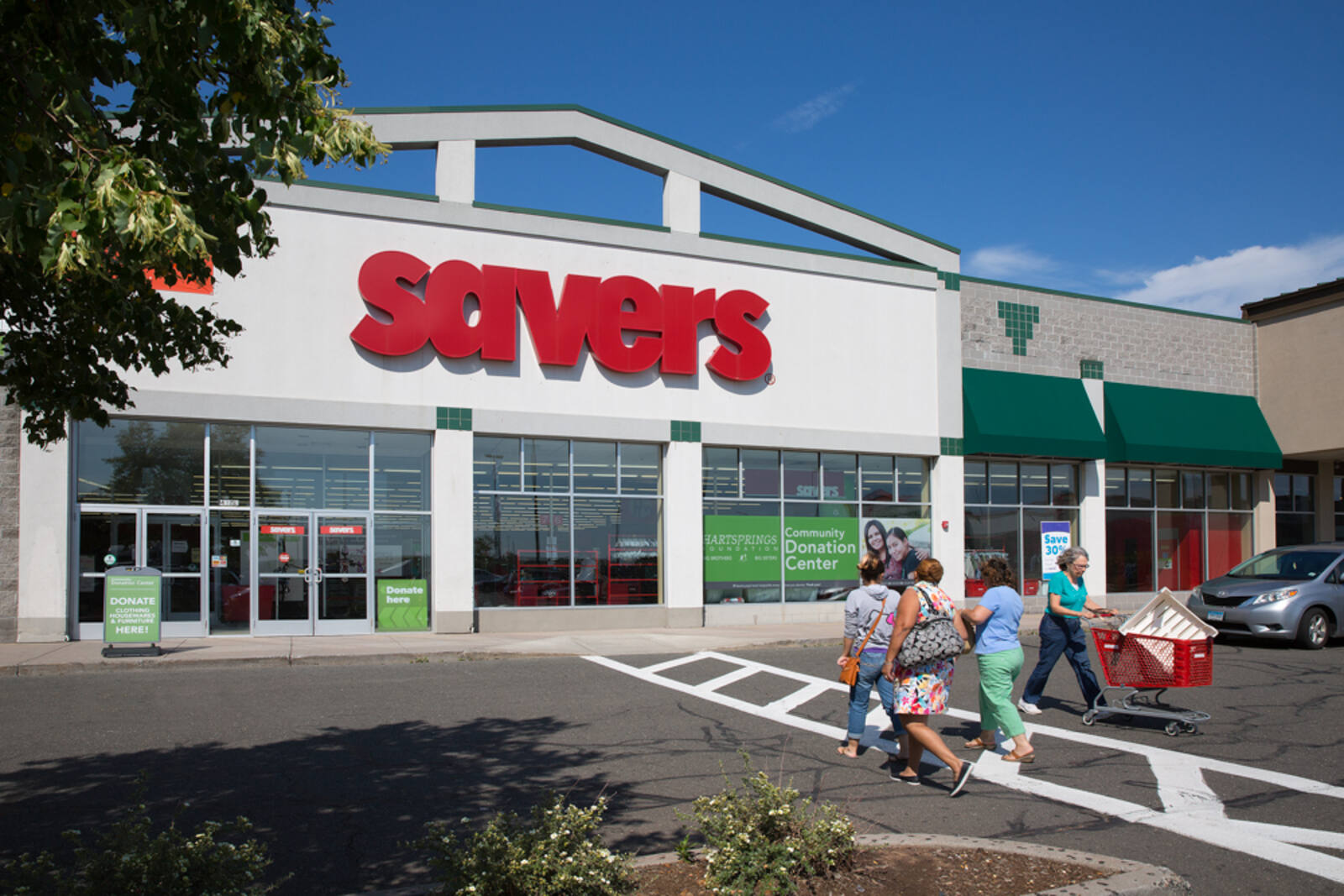 Three people walking towards the entrance of Savers and one person with a shopping cart walking in the opposite direction.