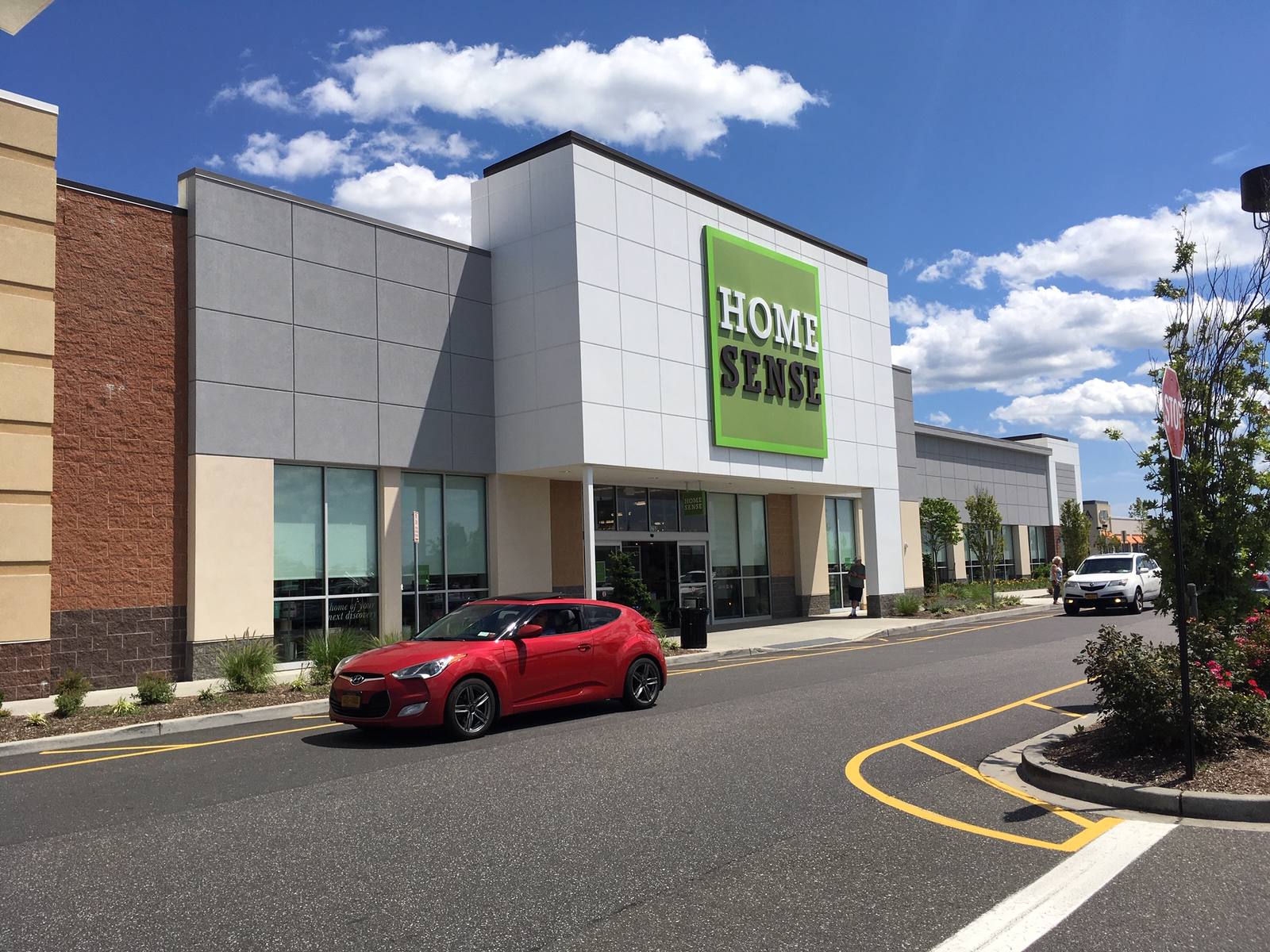 Red car passing by Home Sense on a sunny day