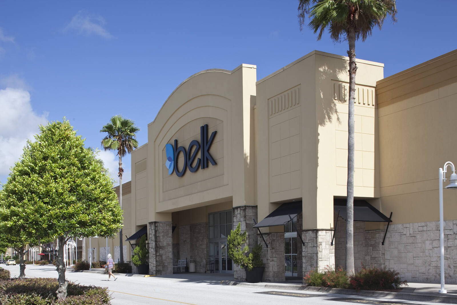 Belk store with trees and palm trees on side with bright blue sky.