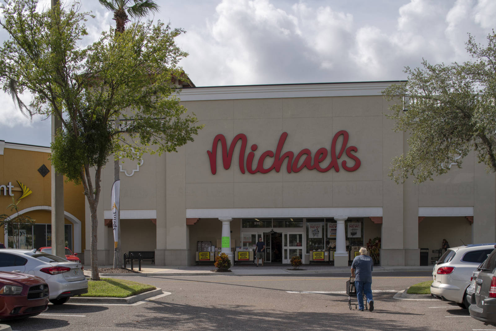 Man with shopping cart enters a tree-lined Michael's storefront.