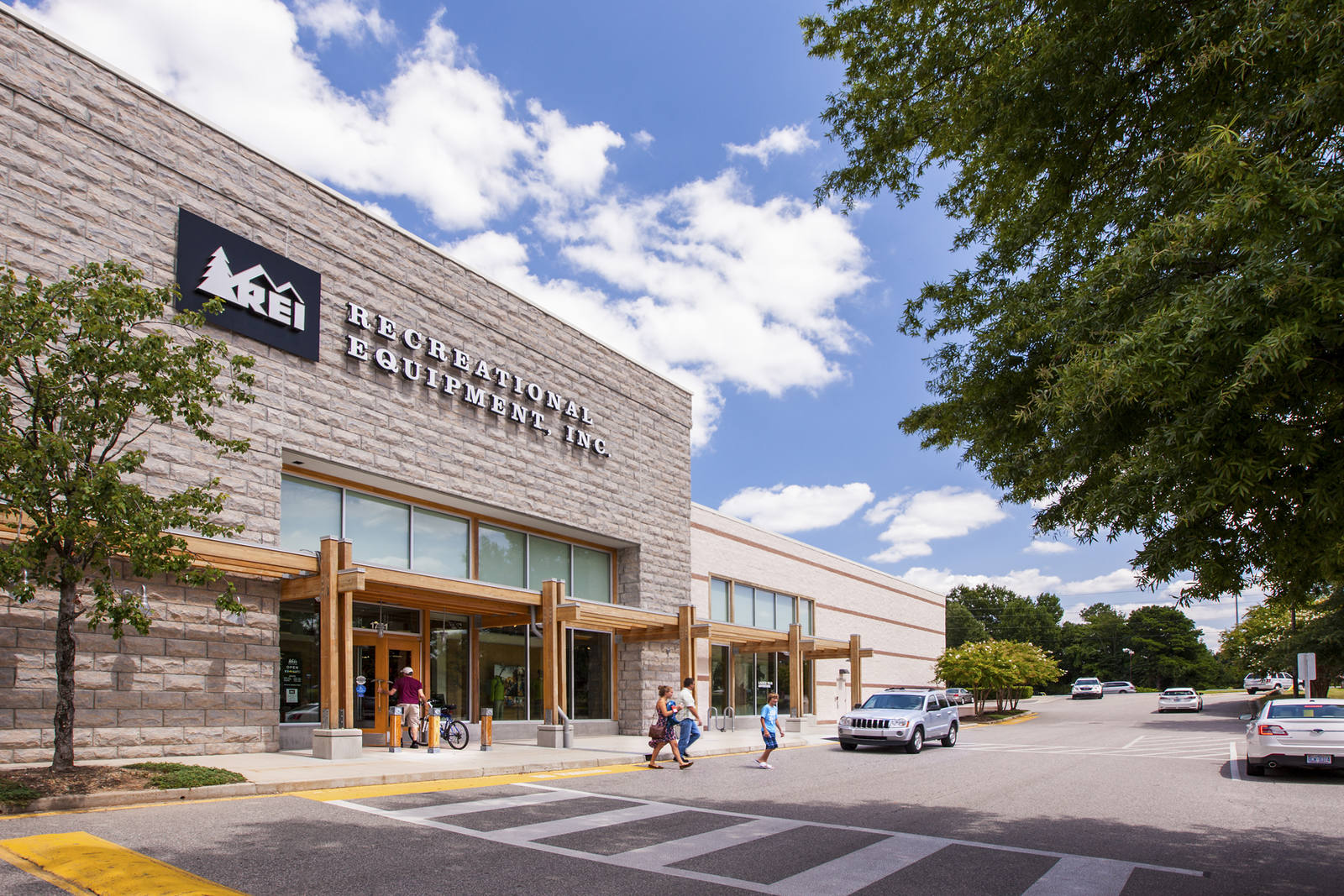 Shoppers exiting REI in tree-lined crosswalk at Devonshire Place.