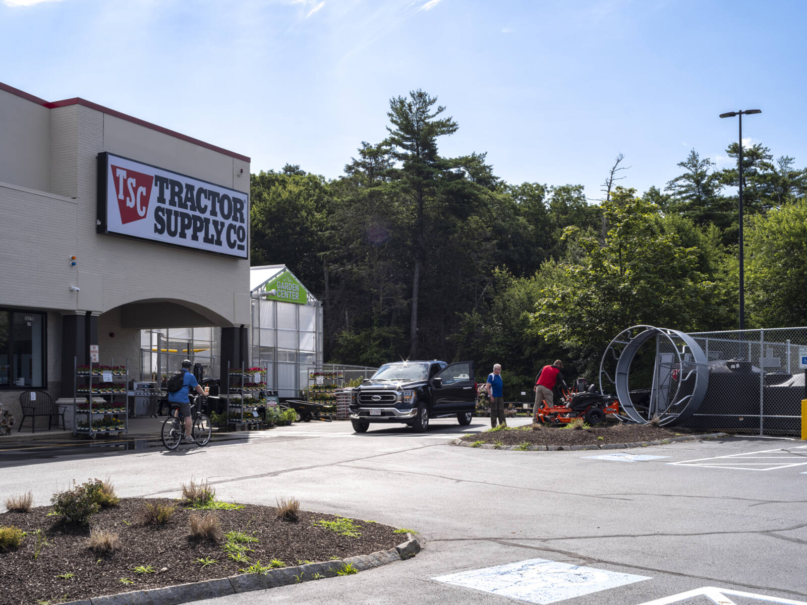 Tractor Supply Co with customers loading truck in front as bicyclist rides by.