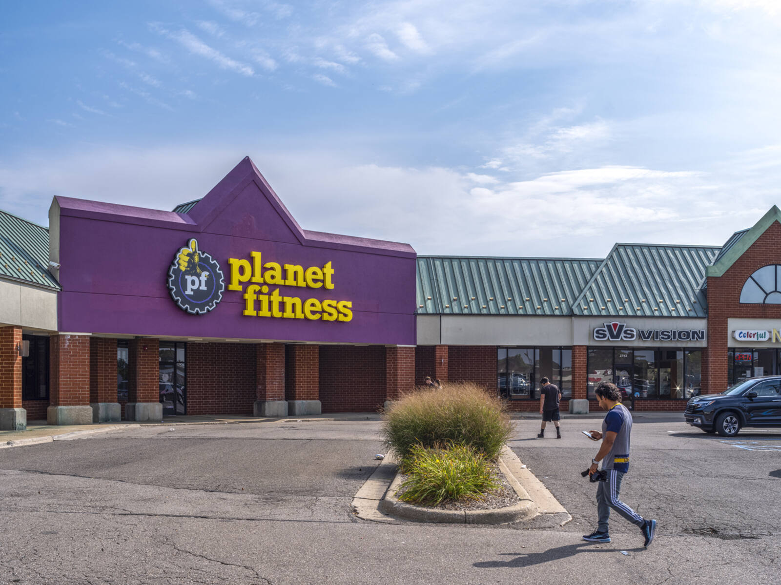 Two men approach Planet Fitness gym via the parking lot.