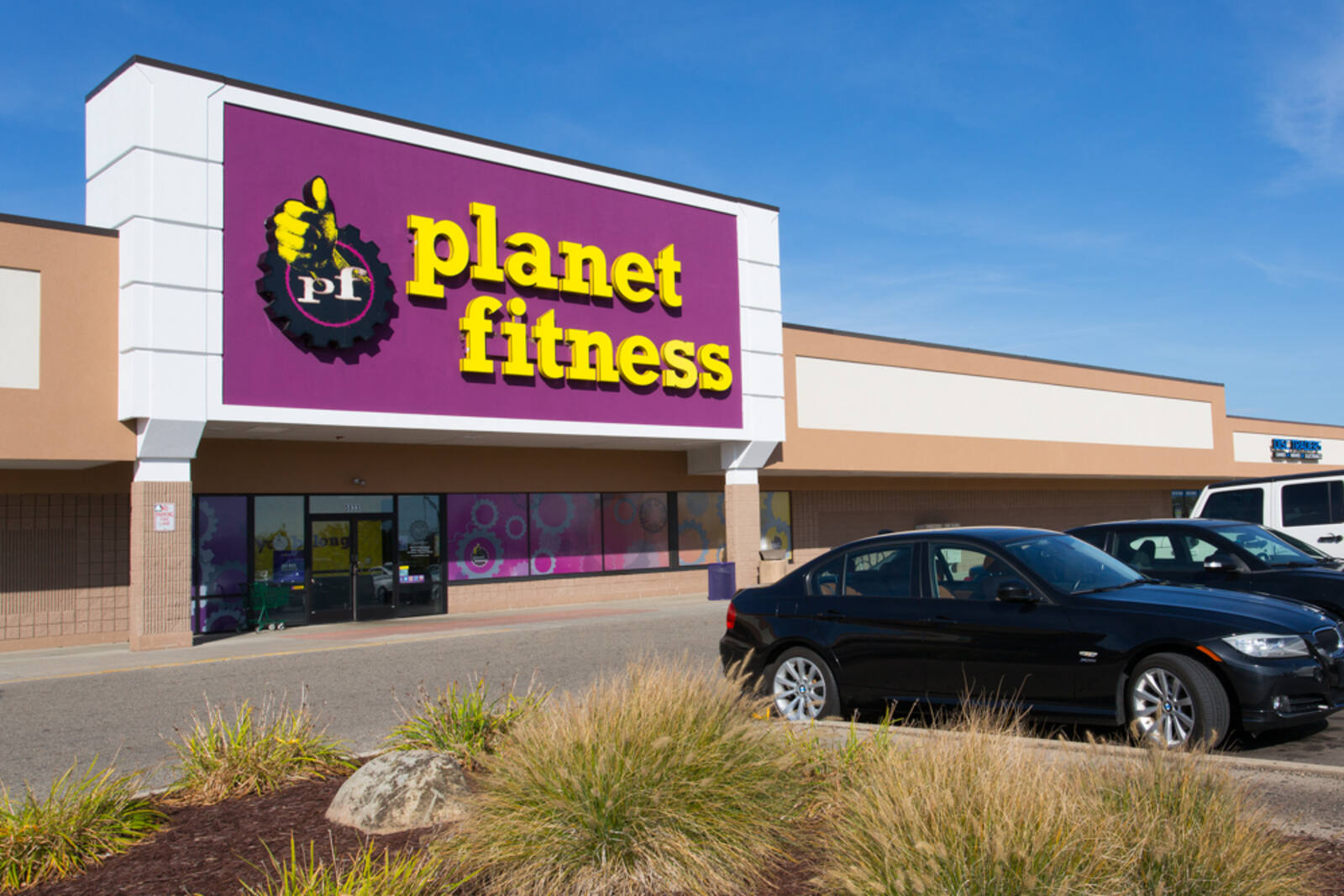 Shrubs and cars in the lot in front of Planet Fitness gym at Delta Center.