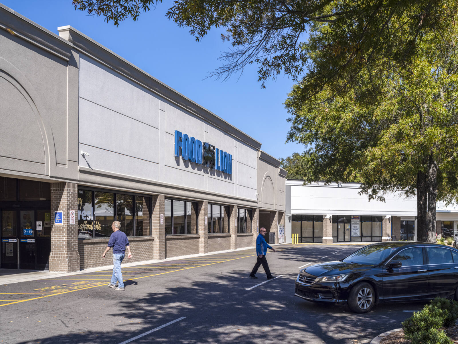 Man enters and another man exits Food Lion with trees and parking lot in front.