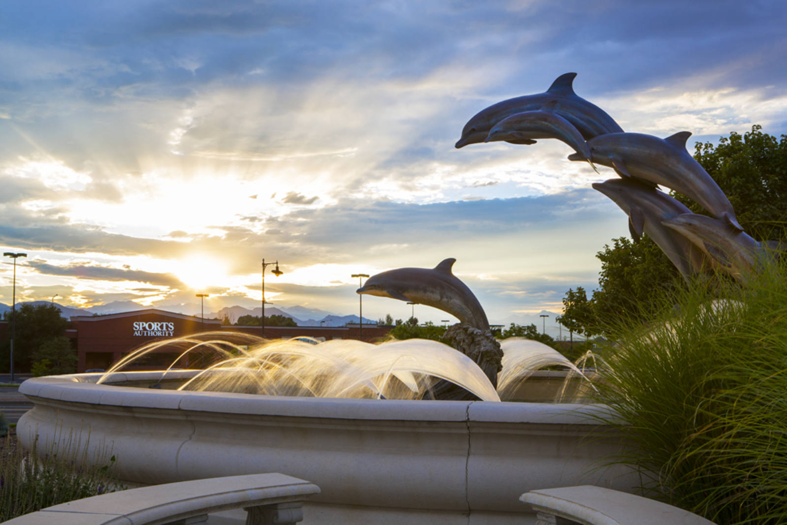 Sun rising over a water fountain with multiple dolphin sculptures