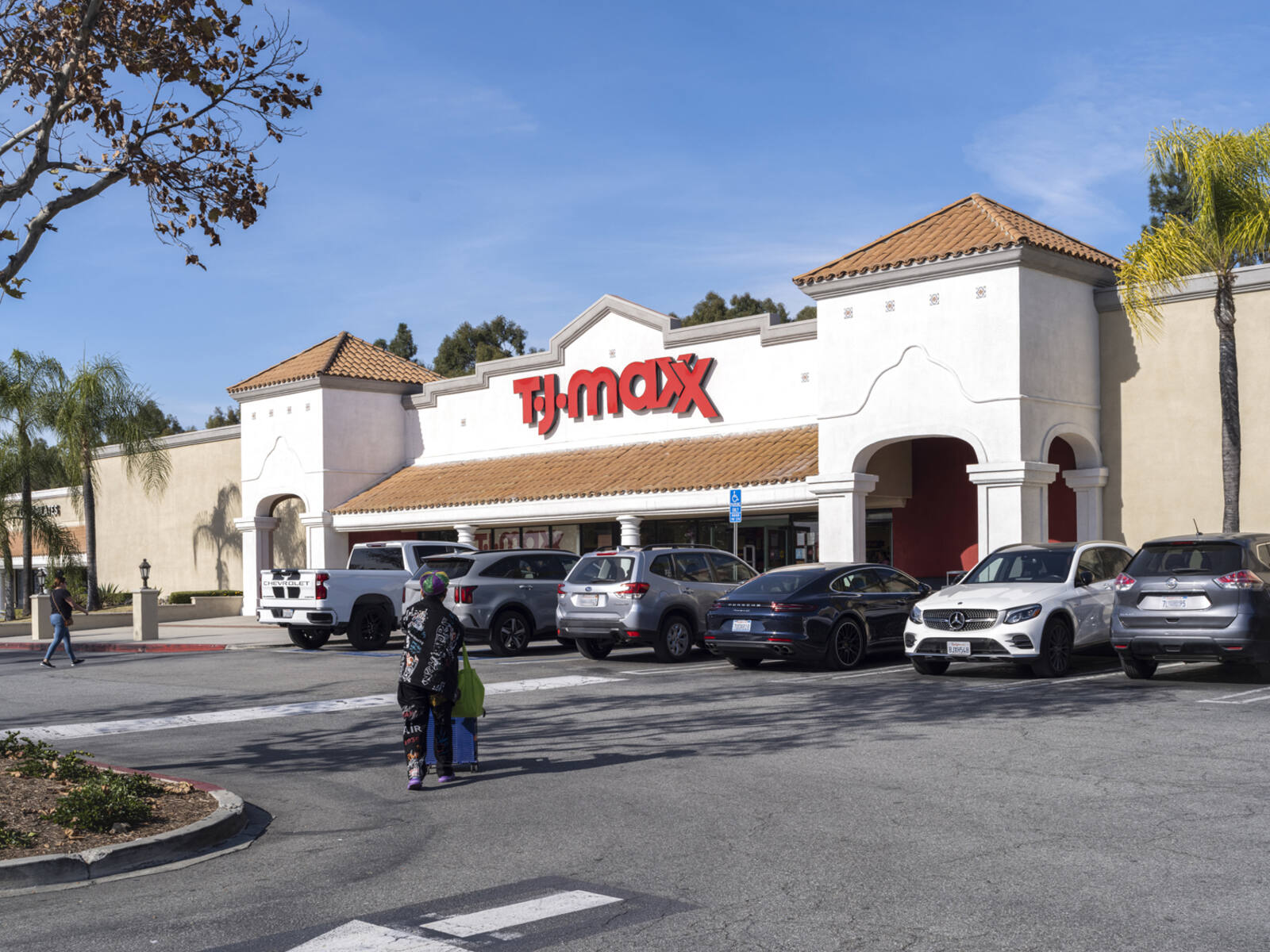 Woman with bags approaches TJ Maxx store at the start of the parking lot.