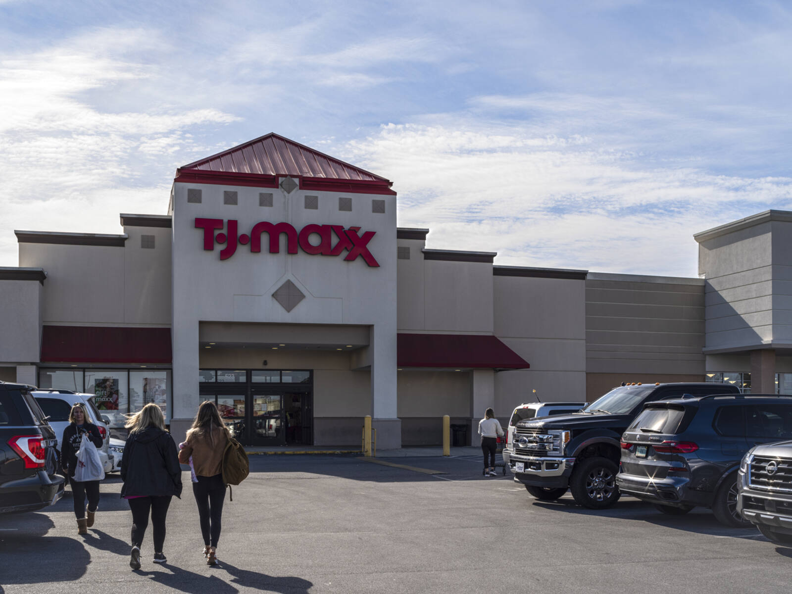 Group of customers approaching TJ Maxx entrance through parking lot of shopping center.