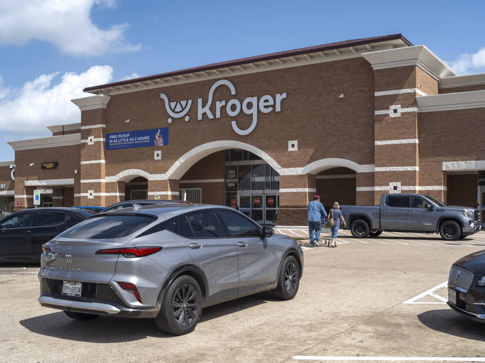 Grey car and couple pushing cart in front of Kroger store.