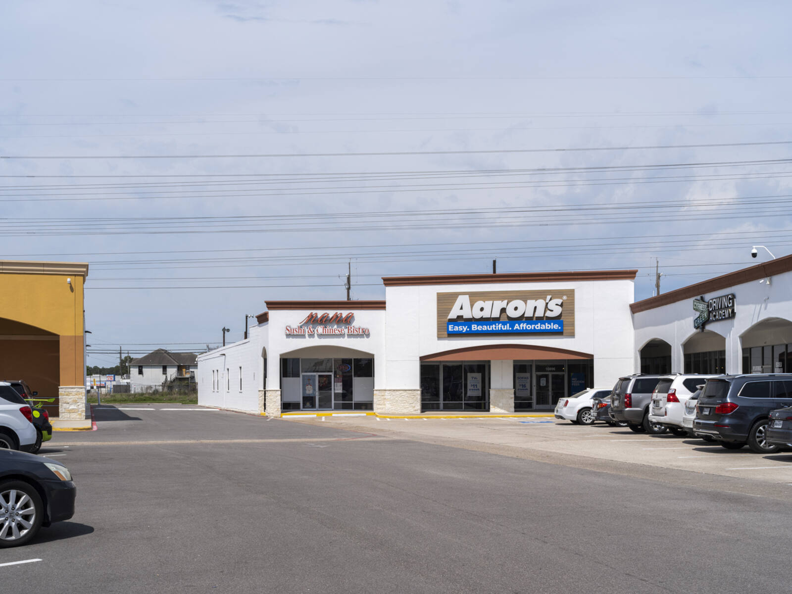 Aaron's furniture store with road in front and parked cars in lot to the right and left.