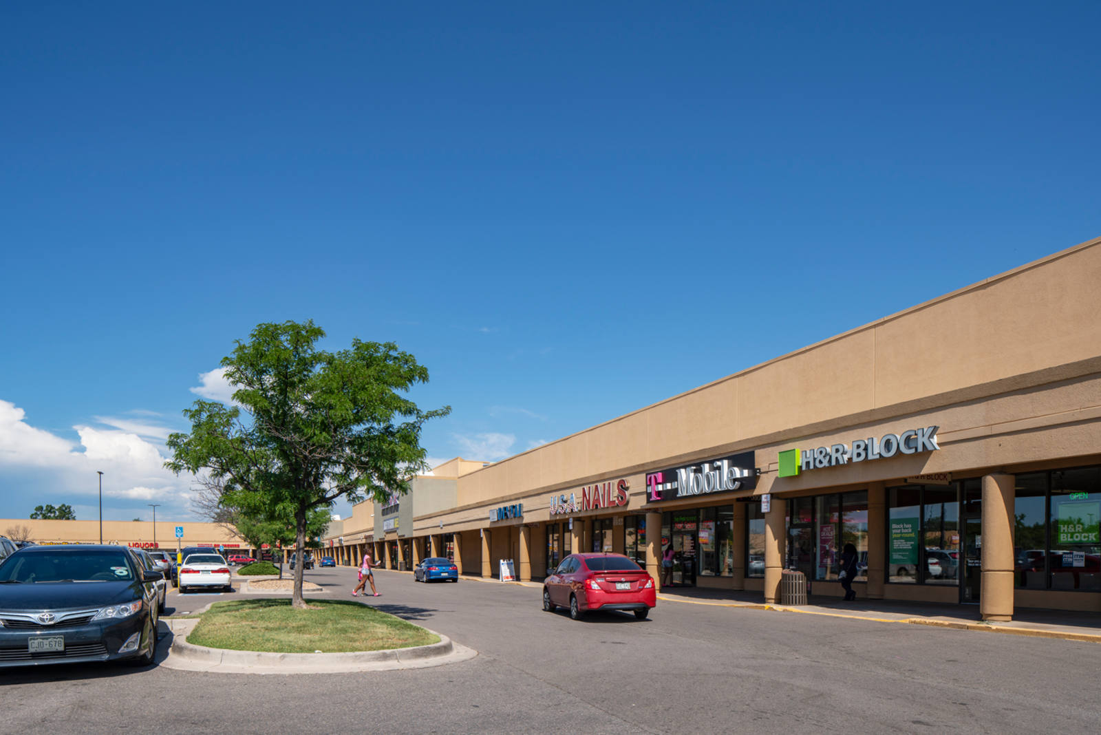 HR Block, T-Mobile and other retail shops at tree-line parking lot in Aurora Plaza.