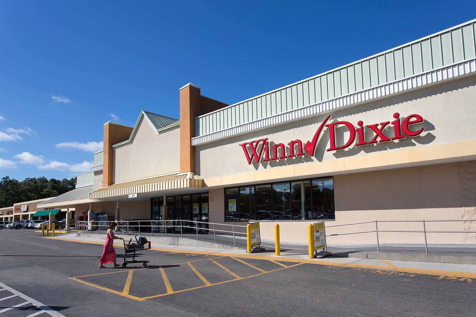 Woman pushing cart towards Winn Dixie supermarket at Normandy Square.