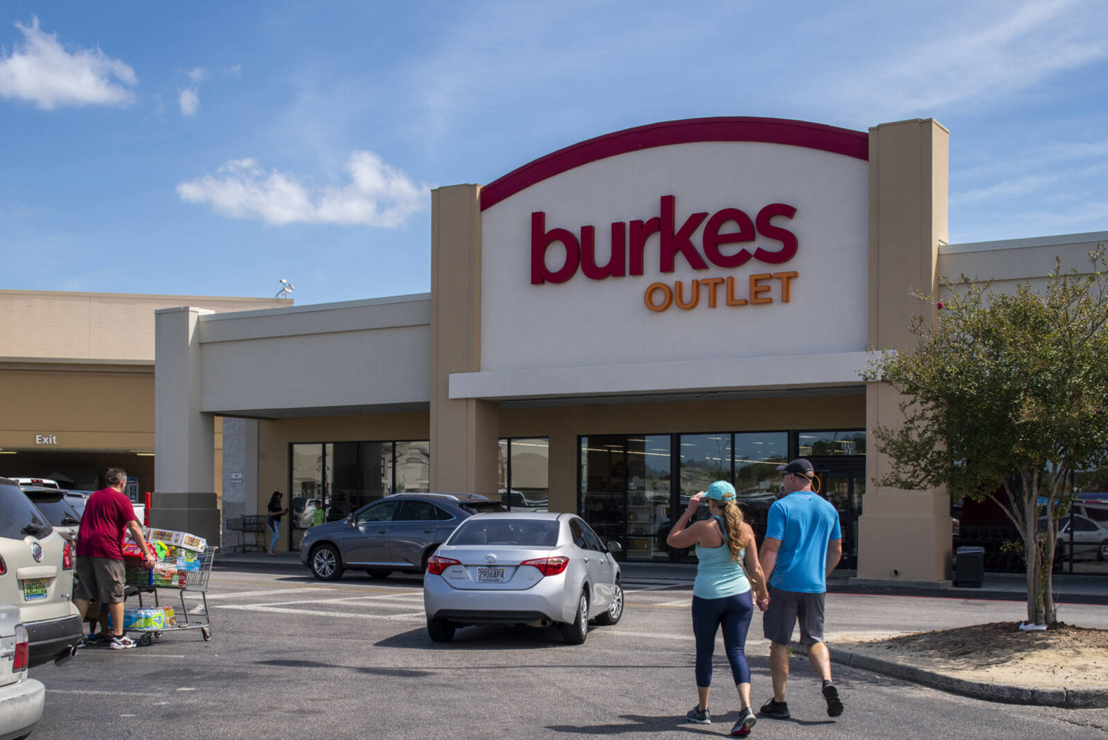 Silver car in between a couple and person with shopping cart at Burkes Outlet