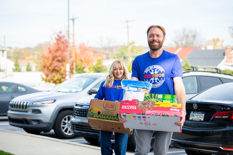 A male and female employee, wearing Brixmor shirts, carrying boxes with food drive donations