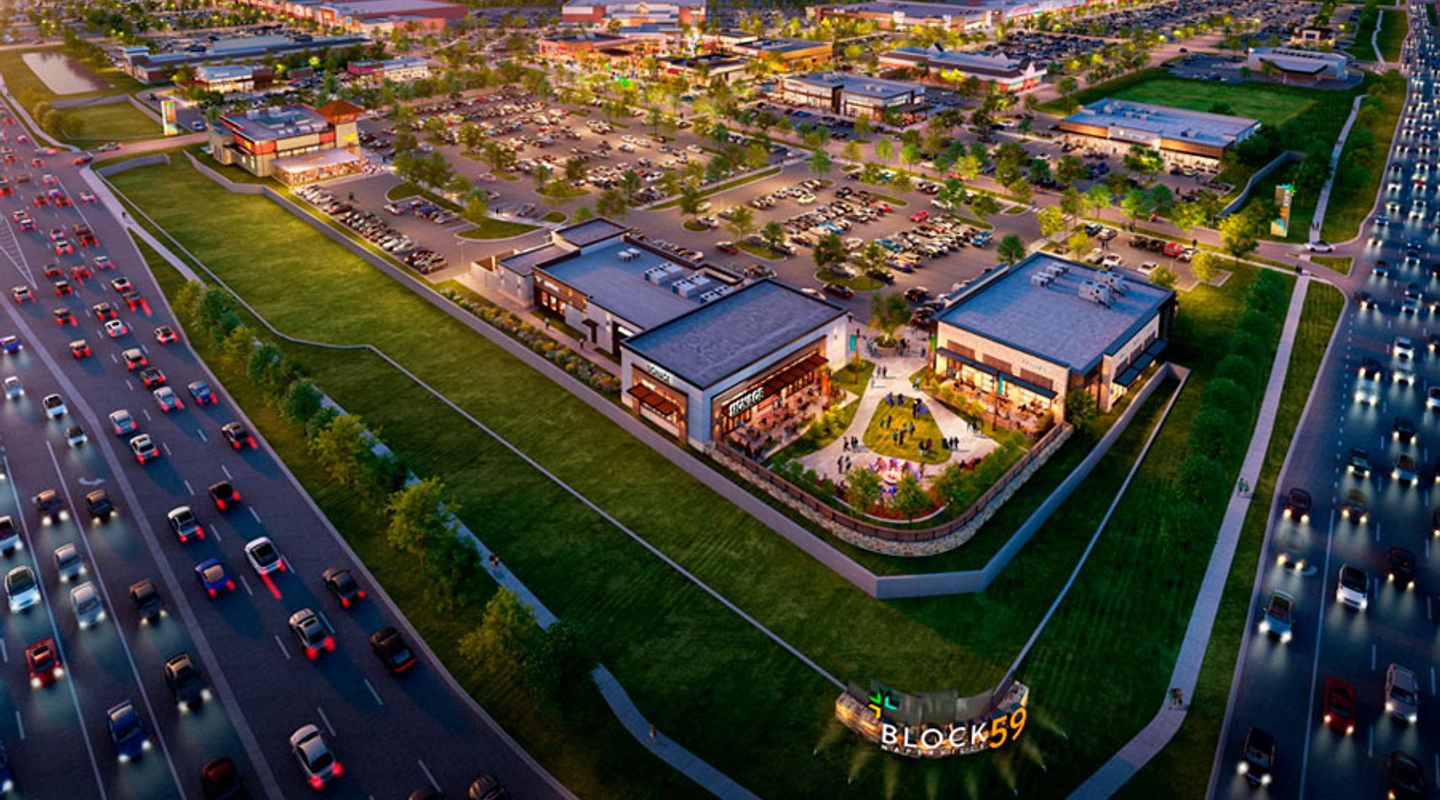 Aerial twilight rendering of Block 59 in Naperville, IL, showcasing the full mixed‑use development with multiple restaurant and retail buildings, illuminated pedestrian areas, landscaped open spaces, extensive parking fields, and adjacent highway traffic flowing along the site’s frontage.
