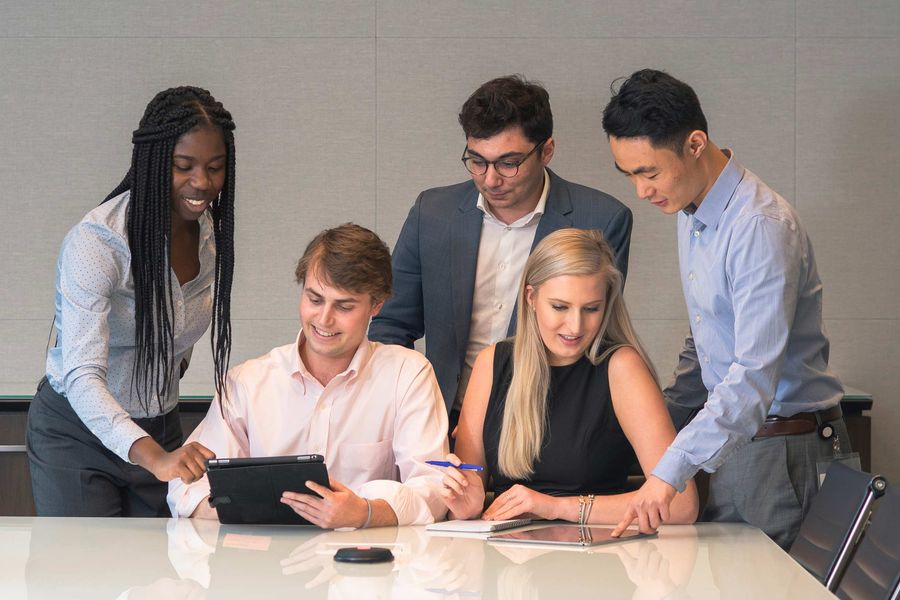 Group of five college interns working at a table with iPads in an office setting