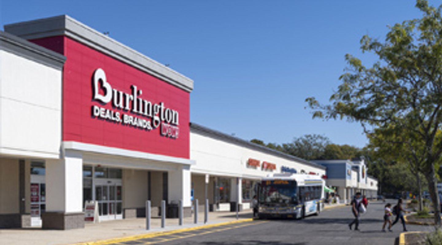 Burlington store and adjacent retailers at College Plaza in Selden, NY, with a public transit bus and pedestrian activity along the main drive aisle of the shopping center.