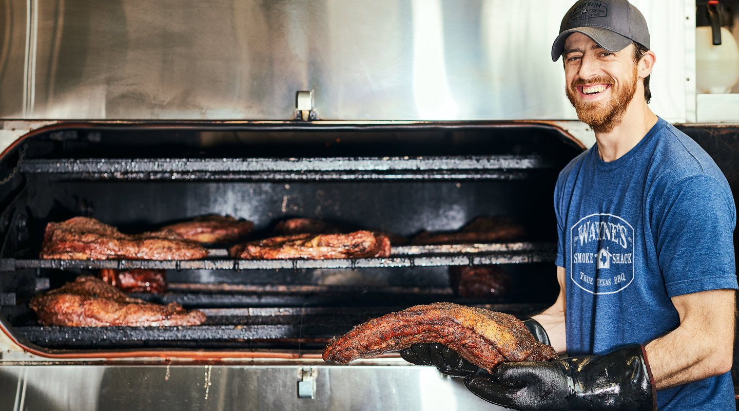 A male restaurant owner pulling meat out of a smoker in a BBQ restaurant
